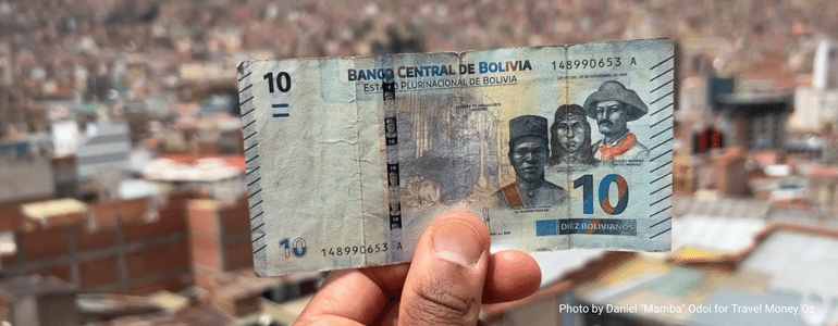 Daniel Mamba Odoi holding up a Bolivian Boliviano note to the Bolivian skyline while travelling South America