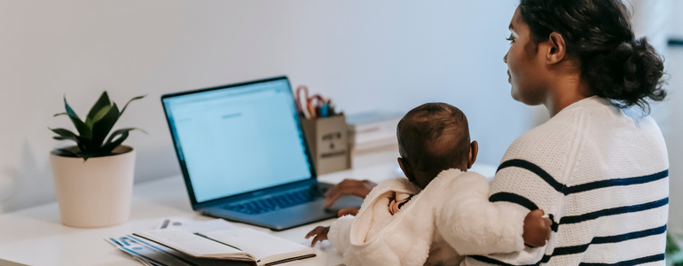 Mother working from home at the computer with her baby on her lap.
